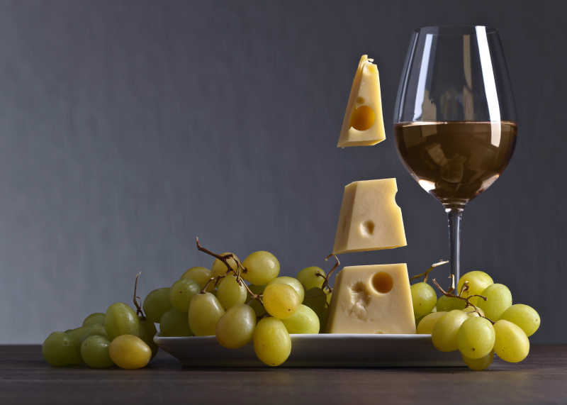 木桌上放着绿葡萄和葡萄酒还有奶酪