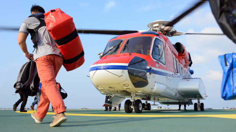 旅客携带行李在石油钻塔平台上乘坐直升飞机
