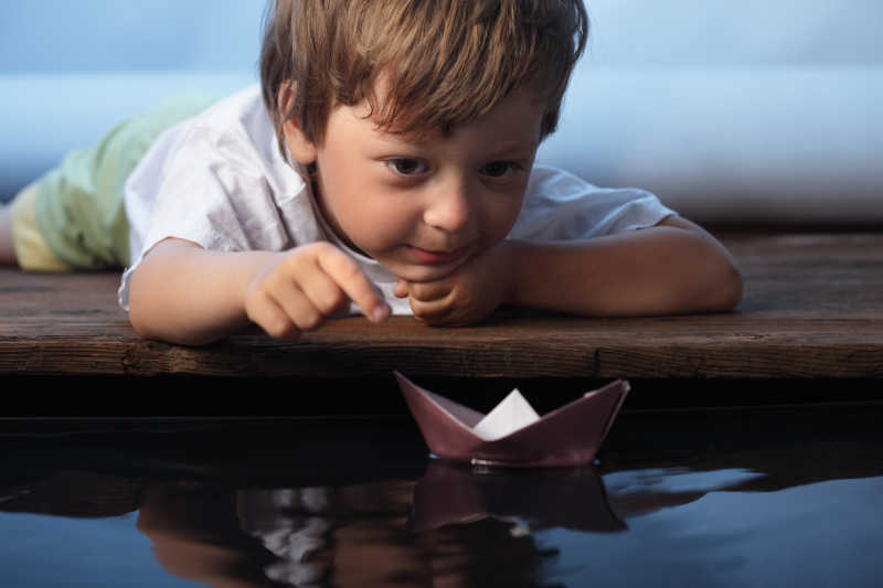 儿童趴着看水里的纸船
