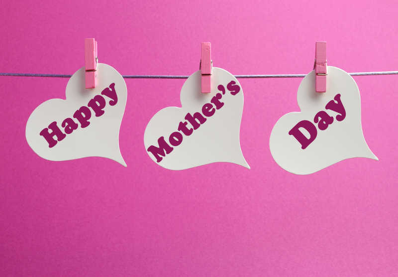 快乐的母亲节白色心形礼物标签挂在钉子上的粉红色背景