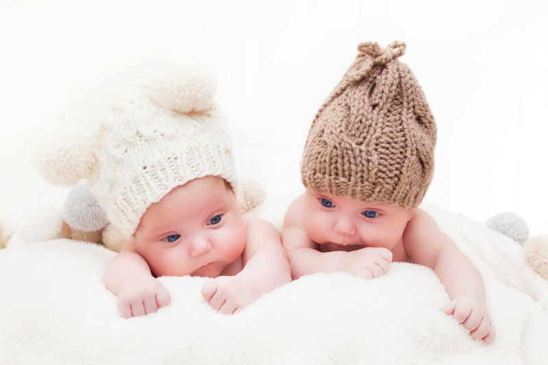 戴着羊毛绒球帽的双胞胎姐妹的婴儿躺在一起