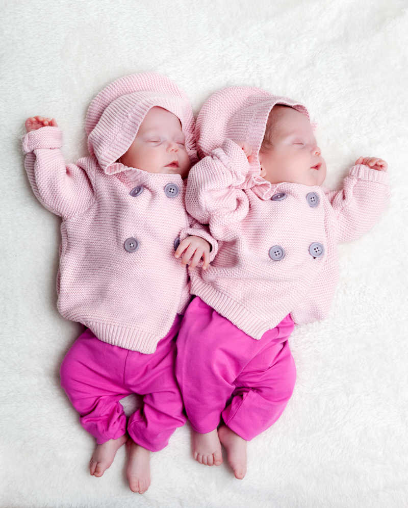 穿着粉红色的毛衣的新生双胞胎姐妹睡在白色的皮毛上