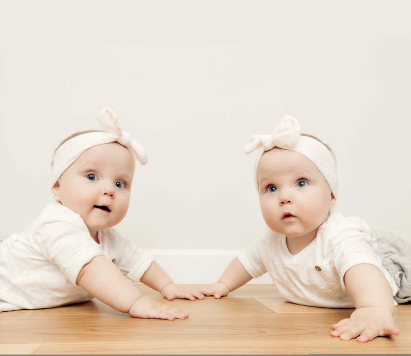 戴着头巾的可爱的双胞胎姐妹一起趴在木地板上