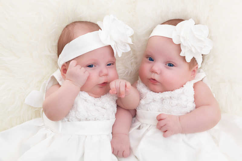 双胞胎姐妹躺在白色柔软的毛毯上