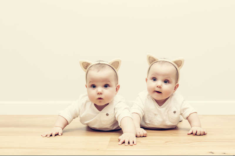 戴着猫耳朵的头巾的可爱的双胞胎姐妹在木地板上