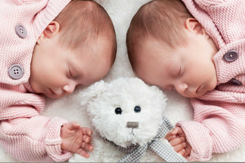新生双胞胎姐妹与玩具熊在白色毯子上睡觉