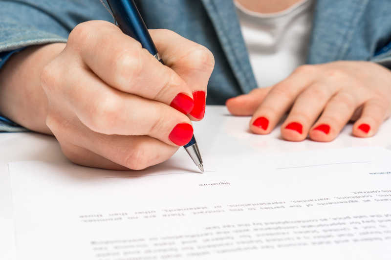 涂了大红色甲油的女性用圆珠笔签合同文件