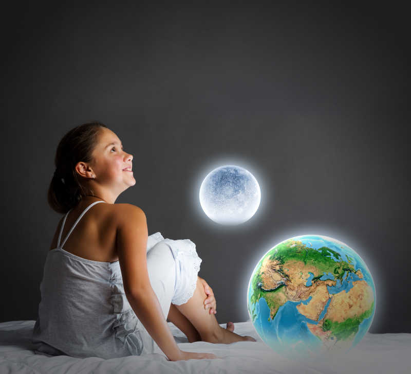 可爱的女孩坐在床上看着地球的行星