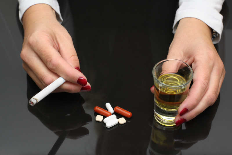 女人举着威士忌拿着香烟和药物在桌子上