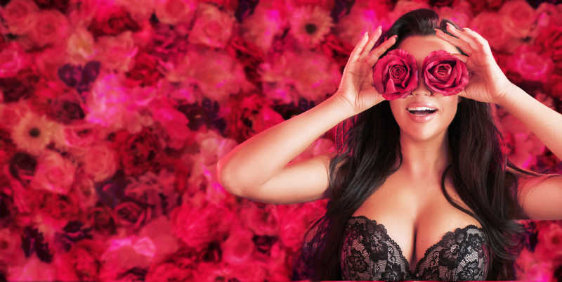 红色花瓣背景下的拿着玫瑰花的时尚性感女模特特写