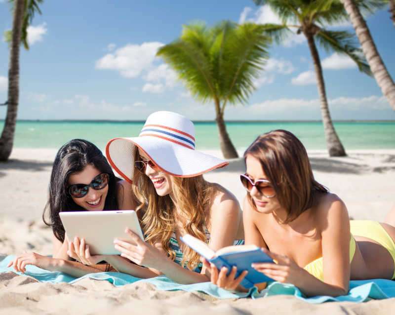 海滩上的三个正在看书和平板电脑的年轻人