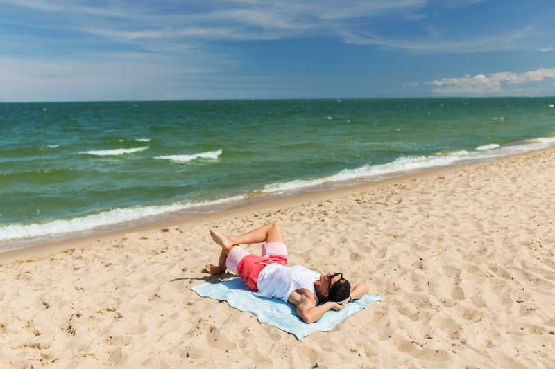 躺在海滩毛巾上晒日光浴的愉快的年轻人