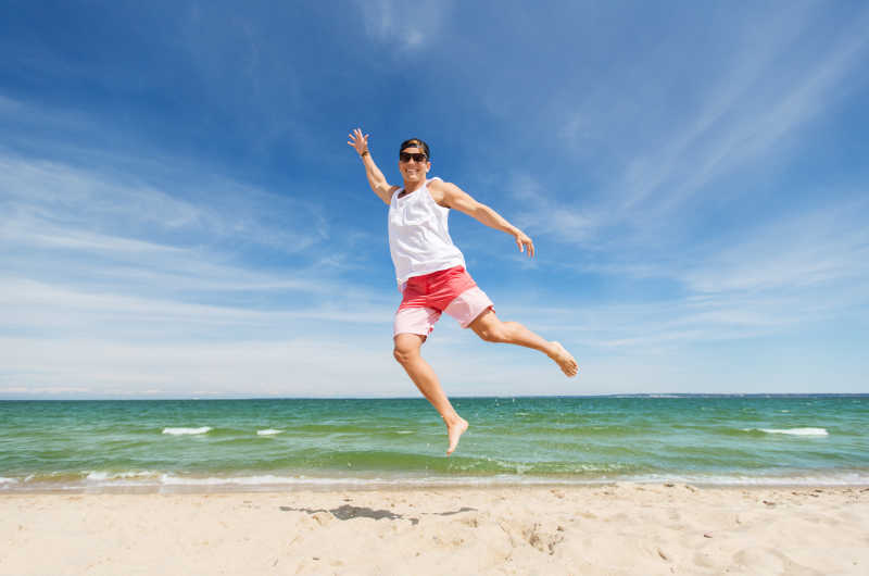 跳跃在夏天海滩上微笑的年轻人