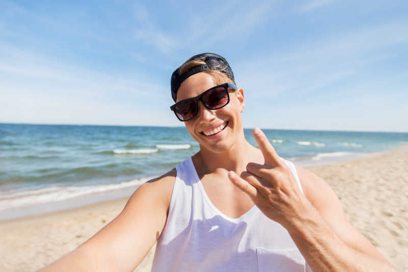 戴着太阳镜在海滩上自拍的年轻人