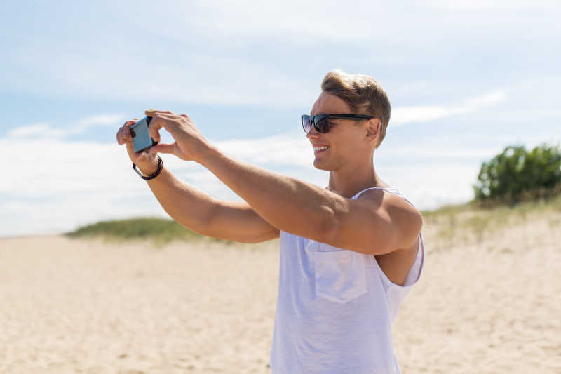 夏天海滩上手拿智能手机拍摄的年轻人