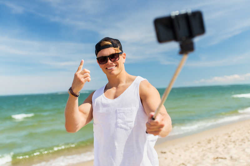 海滩上用智能手机自拍的年轻人