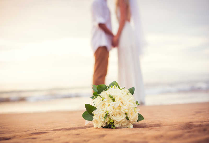海滩上虚化的新娘新郎和捧花特写