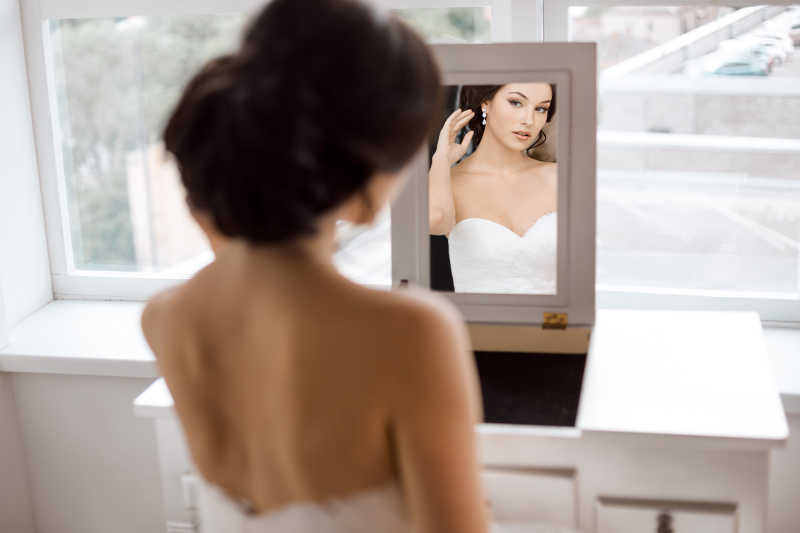 年轻美丽的新娘的肖像在镜子里看着自己