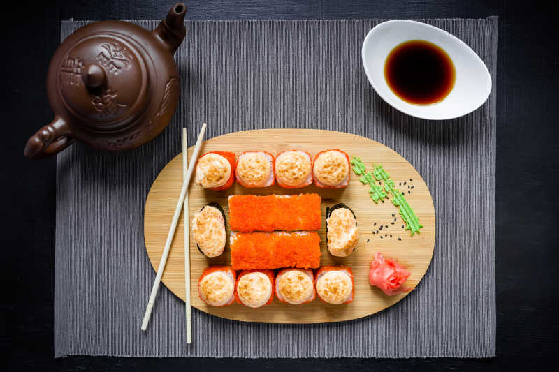 灰色的桌布上一组寿司卷旁边酱油茶杯和筷子