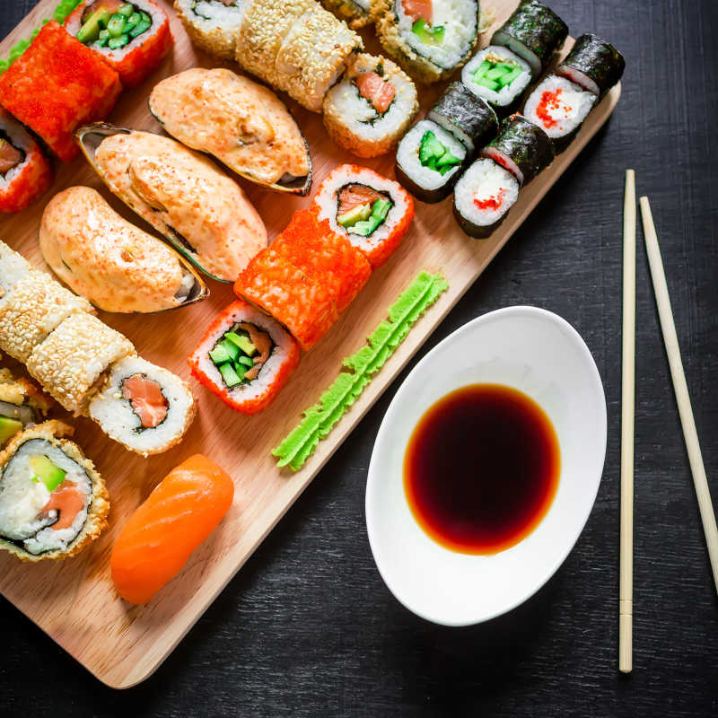 黑色背景上日本的传统食物寿司卷贻贝酱油和筷子