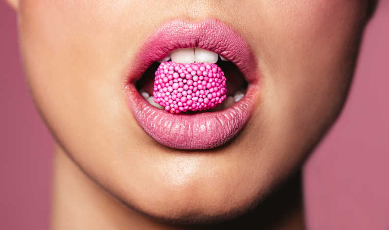 时尚粉红色的嘴唇咬着一块糖果