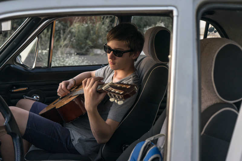 戴着太阳镜的男孩坐在车里弹吉他