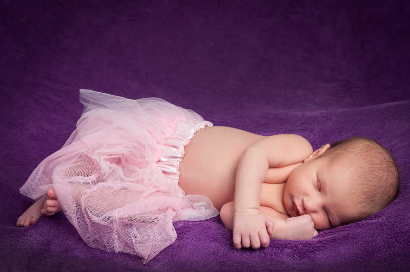 紫色背景下穿着粉色蕾丝裙睡着的婴儿