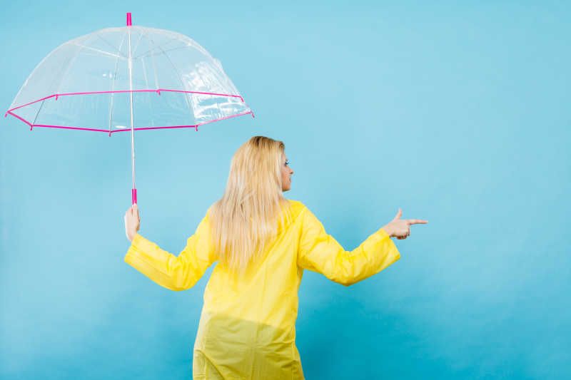 穿着雨衣拿着雨伞手指向另一边的金发女性