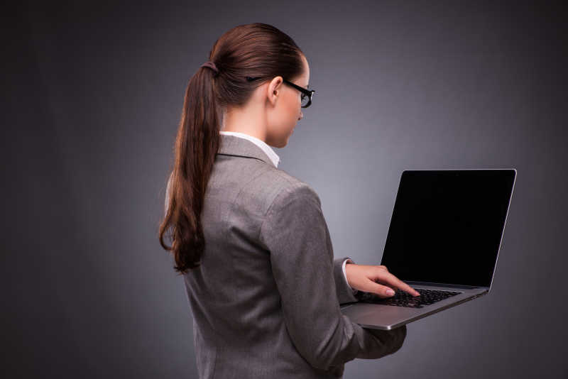 灰色背景下的手拿笔记本电脑指着键盘的女商人