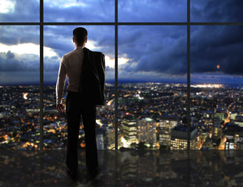 城市夜景下的商人站在窗前看着窗外沉思