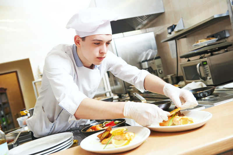 年轻男性厨师穿着白色制服正在摆盘