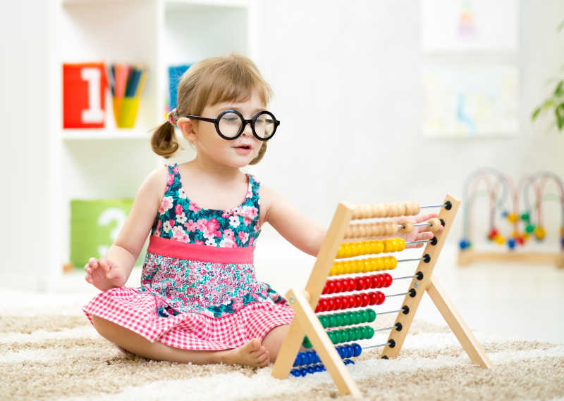室内的孩子戴着眼镜玩珠算玩具