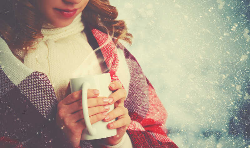 户外寒冷下雪的冬天捧着一杯热咖啡的快乐女人