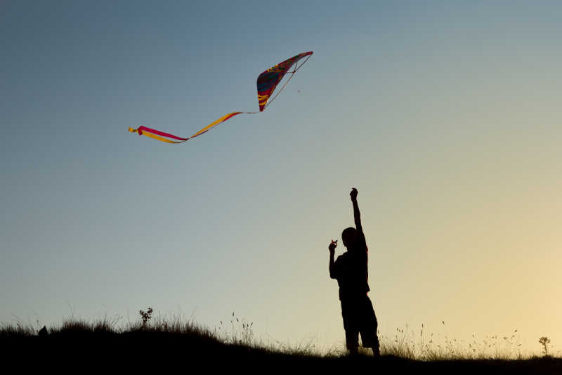 日落时在天空中放风筝的男孩