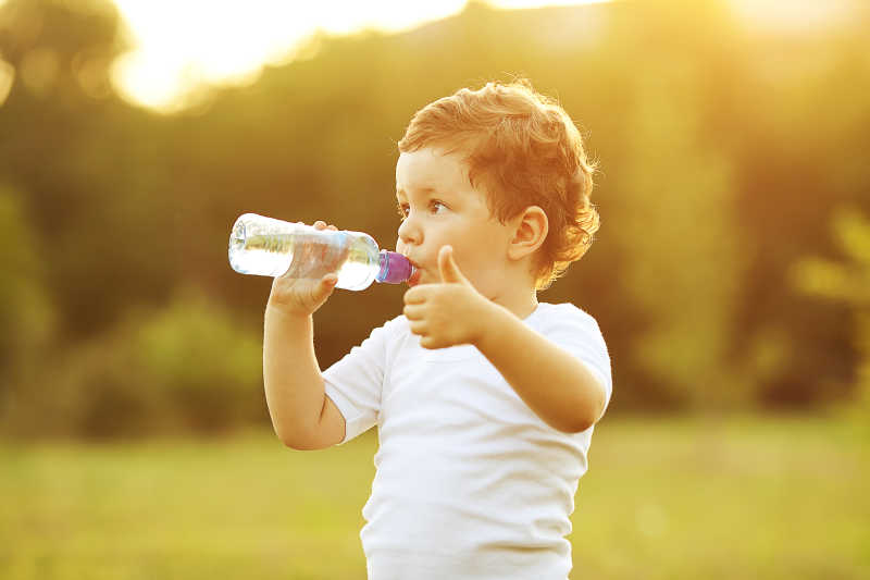 棕色头发的小男孩在公园里喝水并竖起大拇指