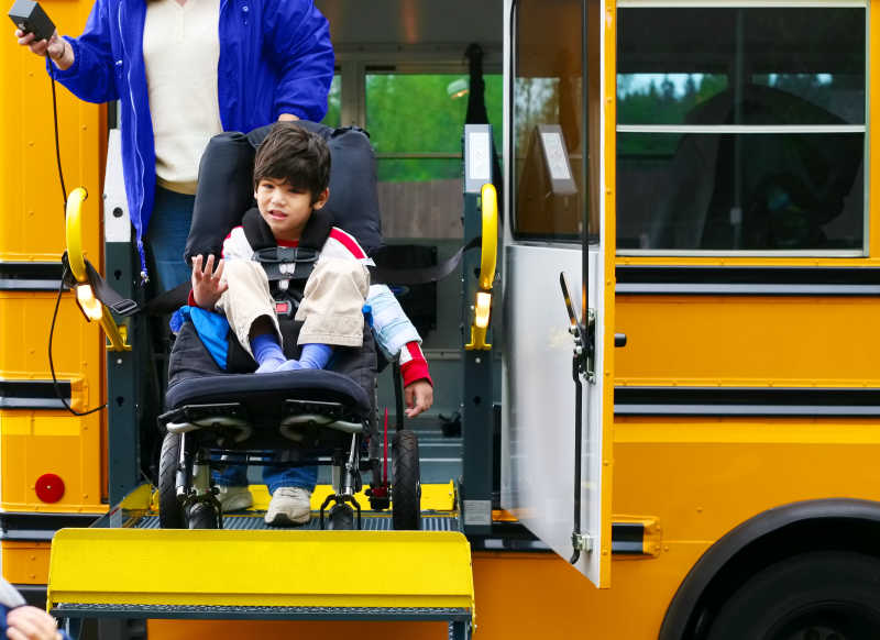 一个残疾的五岁男孩在轮椅上从校车上下来