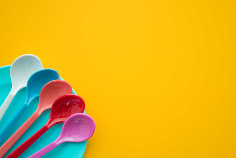 黄色桌子上的蓝色盘子里的五颜六色的勺子