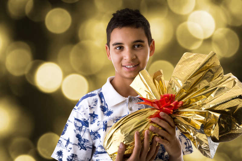 快乐的巴西男孩展示金色包装纸红色蝴蝶结装饰的复活节彩蛋
