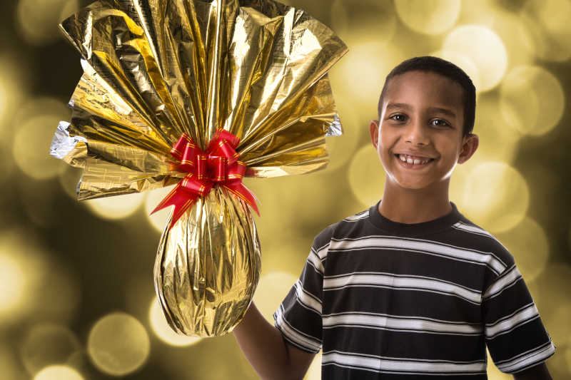 快乐的巴西男孩手举着金色包装纸的复活节彩蛋