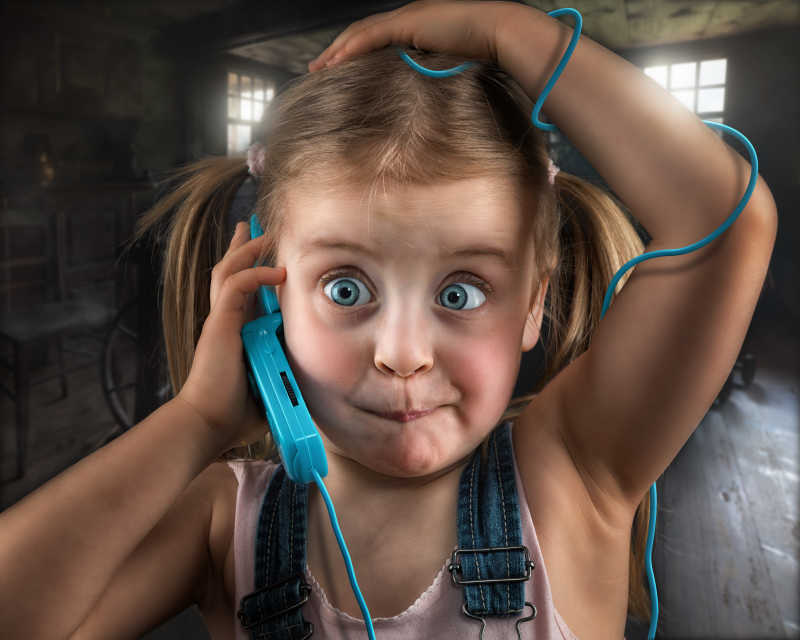 漂亮的小女孩拿着缠绕在身上的线路连接的电话惊讶的睁大眼睛特写