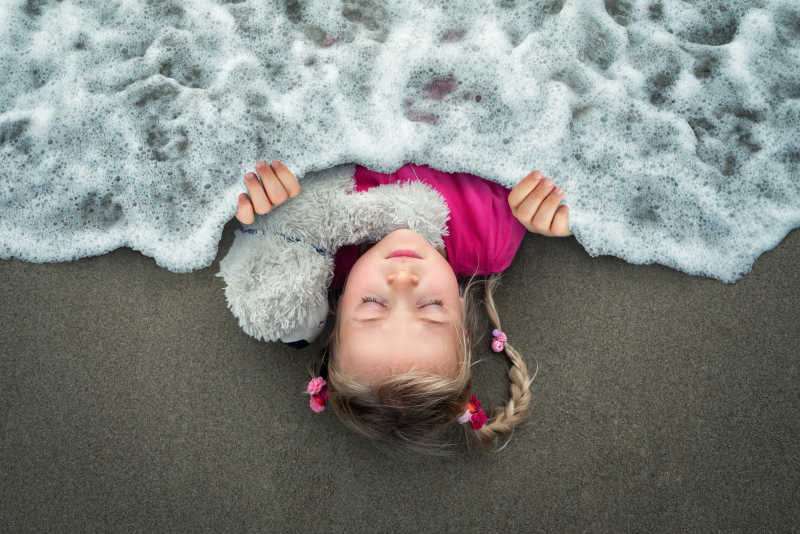 躺在沙滩上想象着把海水波浪当做被子的创意女孩特写