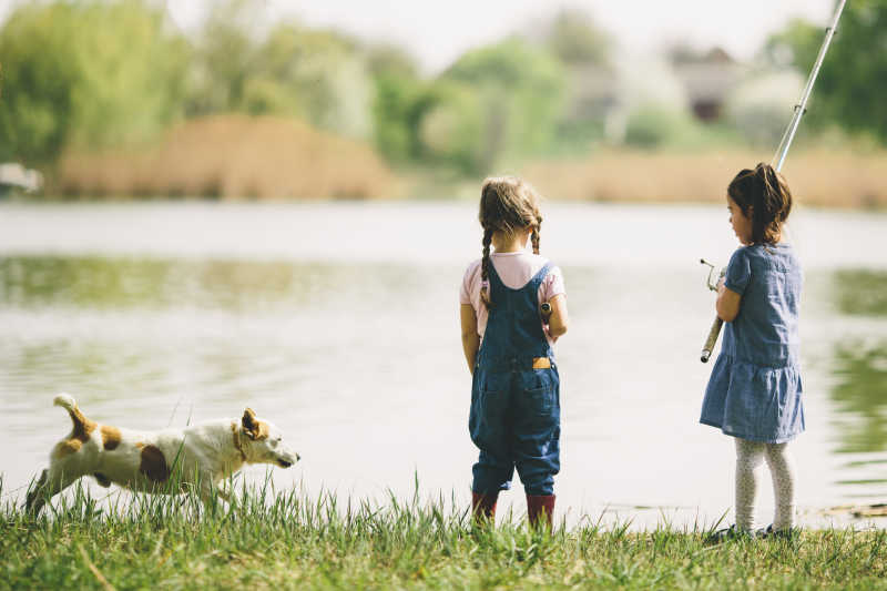 湖边的两个钓鱼的小女孩和狗狗