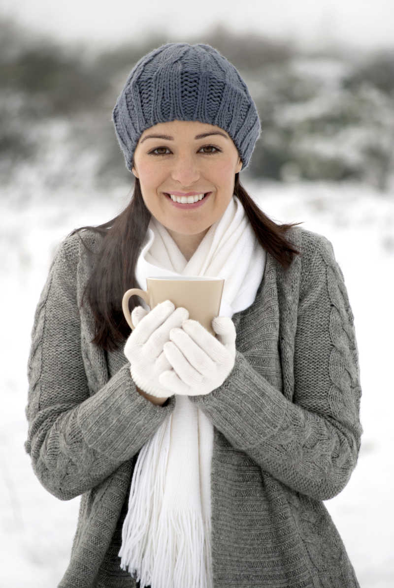 女人在雪地里微笑着喝着热饮料