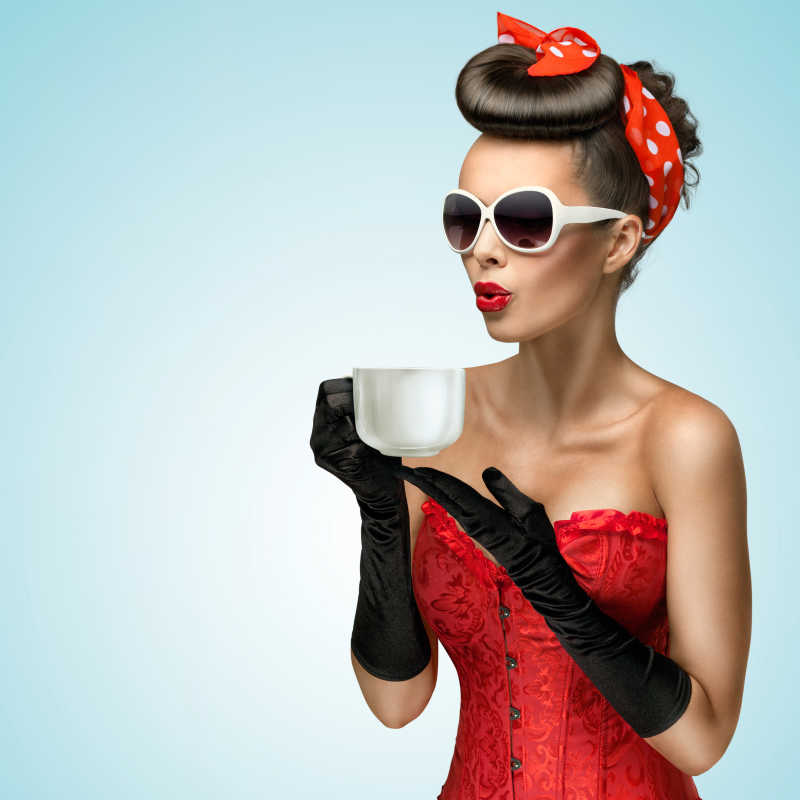 梳着老式头发带着墨镜和老式手套的美女拿着一杯热咖啡