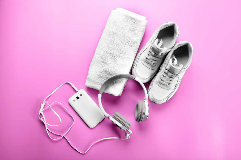 粉红色背景下的运动鞋毛巾和耳机