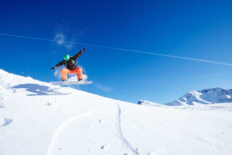 男性的滑雪者穿绿色的头盔黑色的外套和橙色的裤子玩跳在蓝天上滑雪场