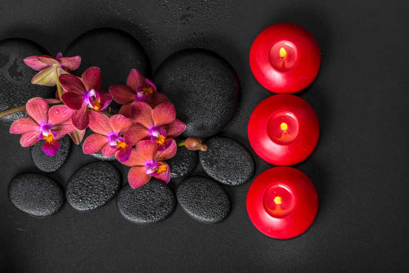 盛开的小枝红兰花蝴蝶兰与水露水和蜡烛上的禅宗玄武岩石头