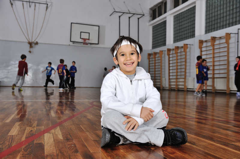一个微笑的小男孩在一群打篮球前面拍照