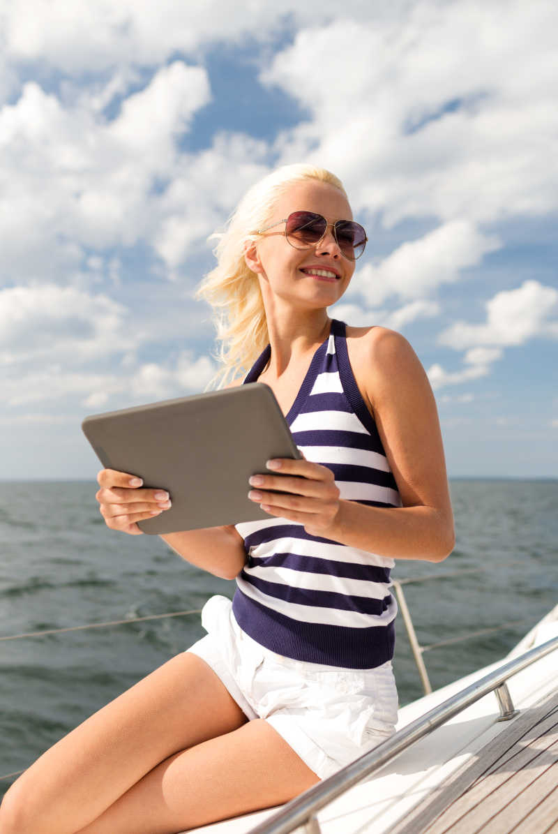 坐在游艇上的微笑女性手拿平板电脑