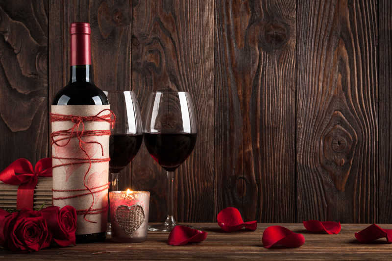 缠着红线的葡萄酒瓶倒着红酒的红酒杯和玫瑰花瓣